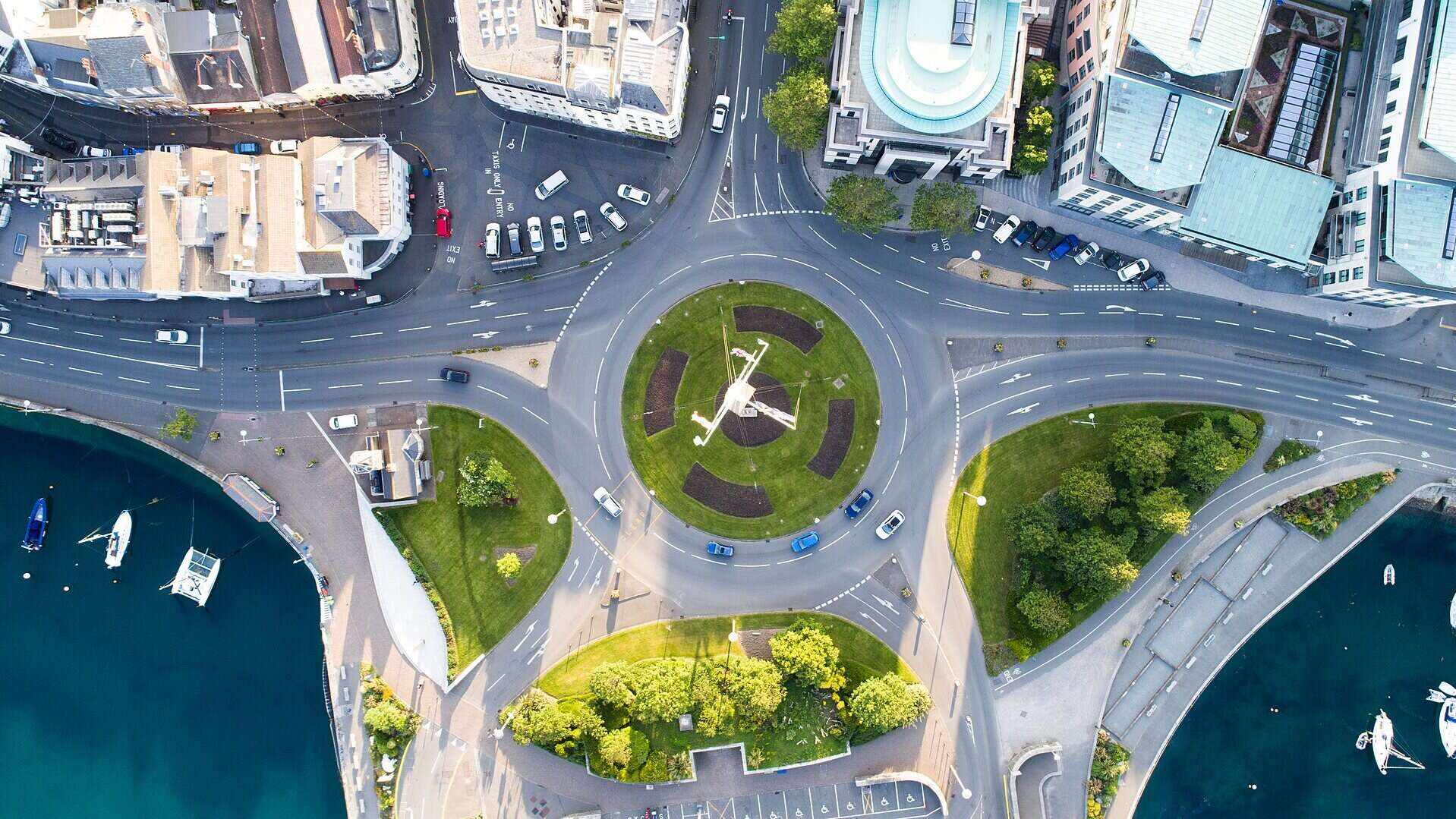 Vista aérea de una rotonda concurrida en una ciudad costera, con el puerto a ambos lados