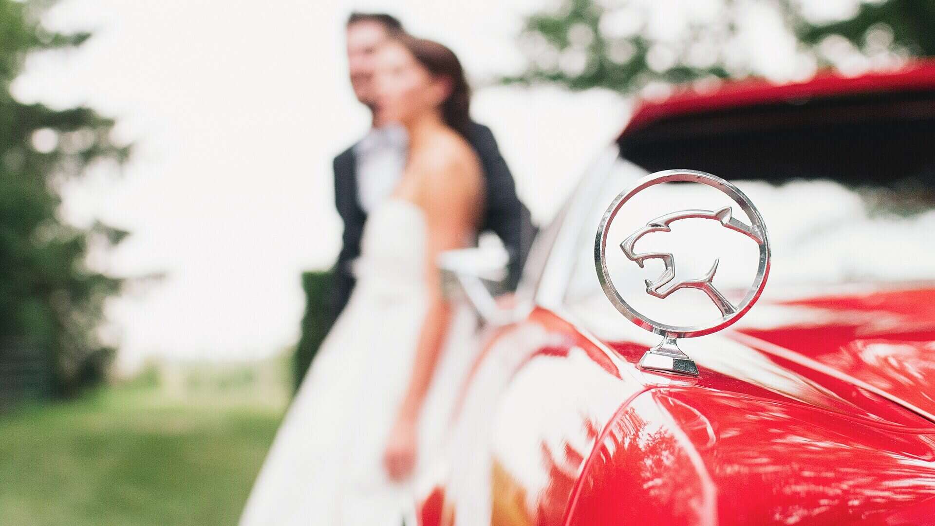 Brautpaar neben einem roten Oldtimer am Hochzeitstag