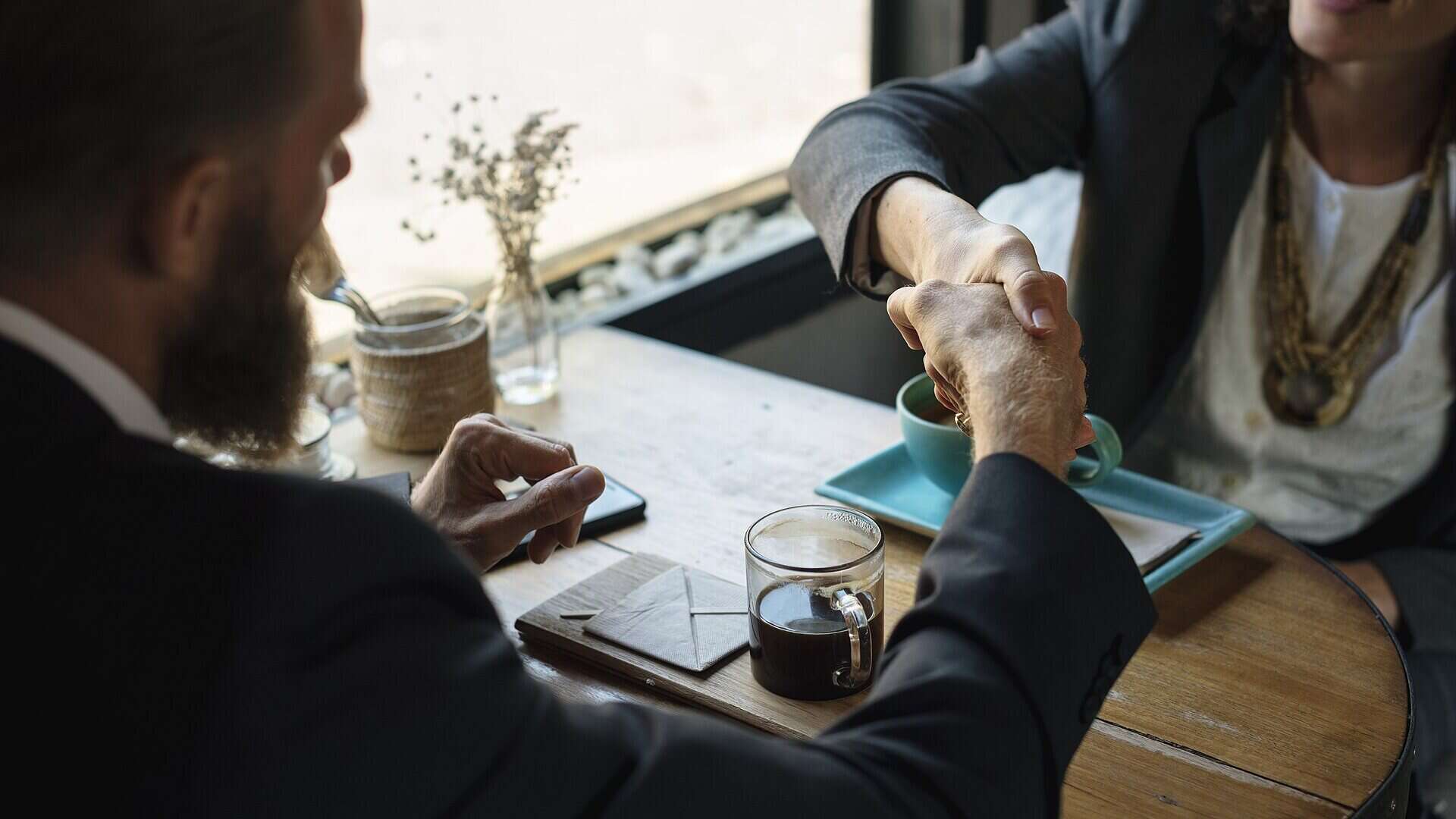 Zwei Personen geben sich an einem Cafétisch nach einer Einigung die Hand